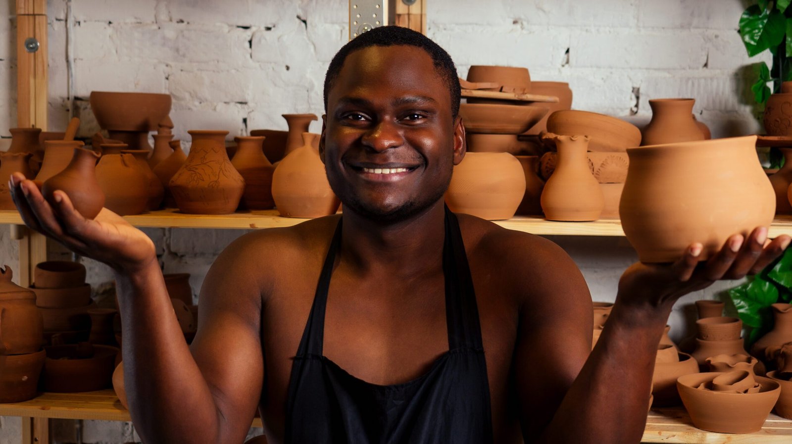 happy African American businessman potter male owner making clay sculpture pot cup vase at workbench in workshop studio . creativity and creative china shop merchant